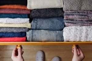 A person opens a wooden drawer filled with neatly folded clothes arranged by color and texture.