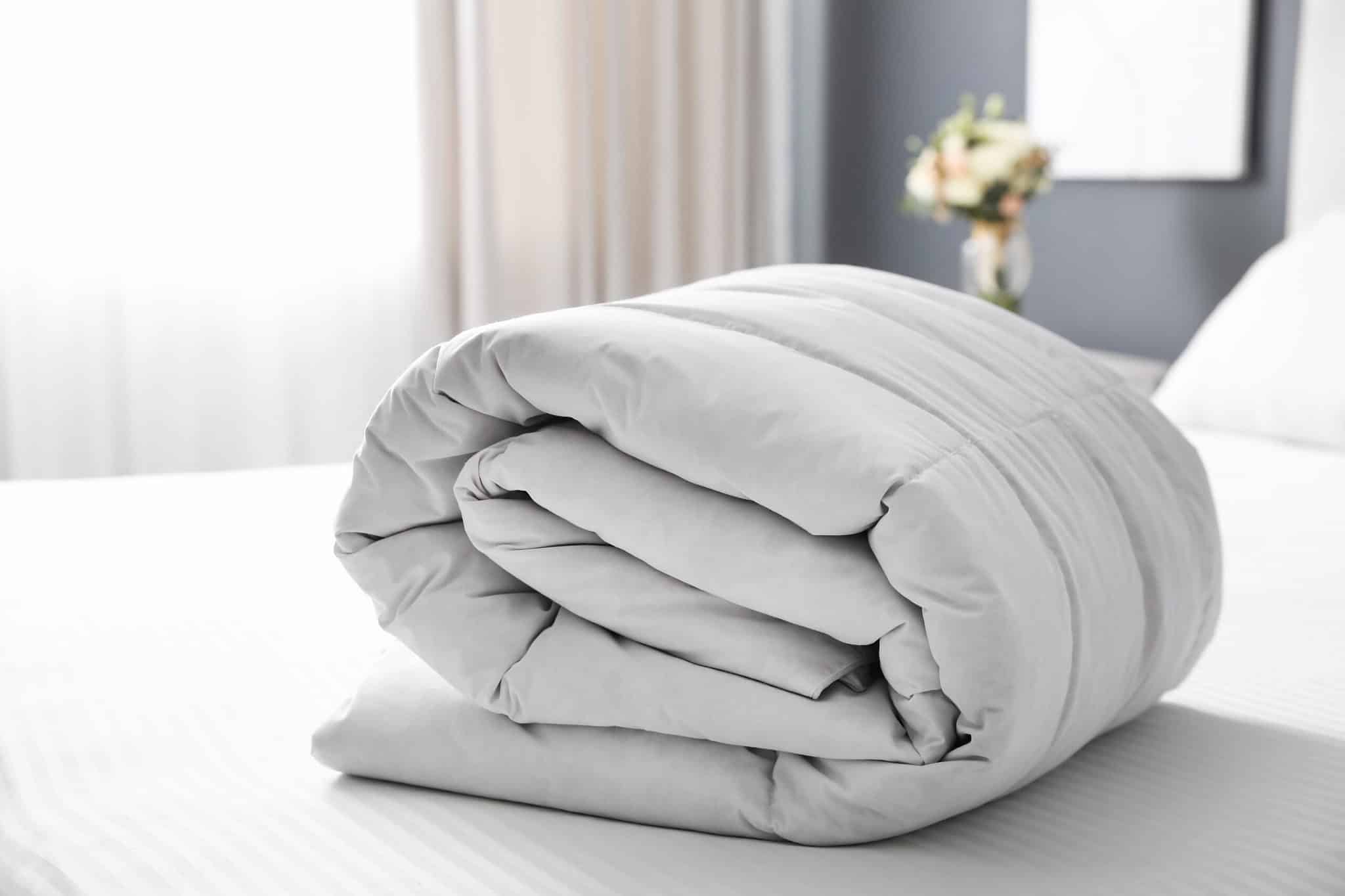 A neatly rolled white comforter placed on a made bed in a bright, modern bedroom.