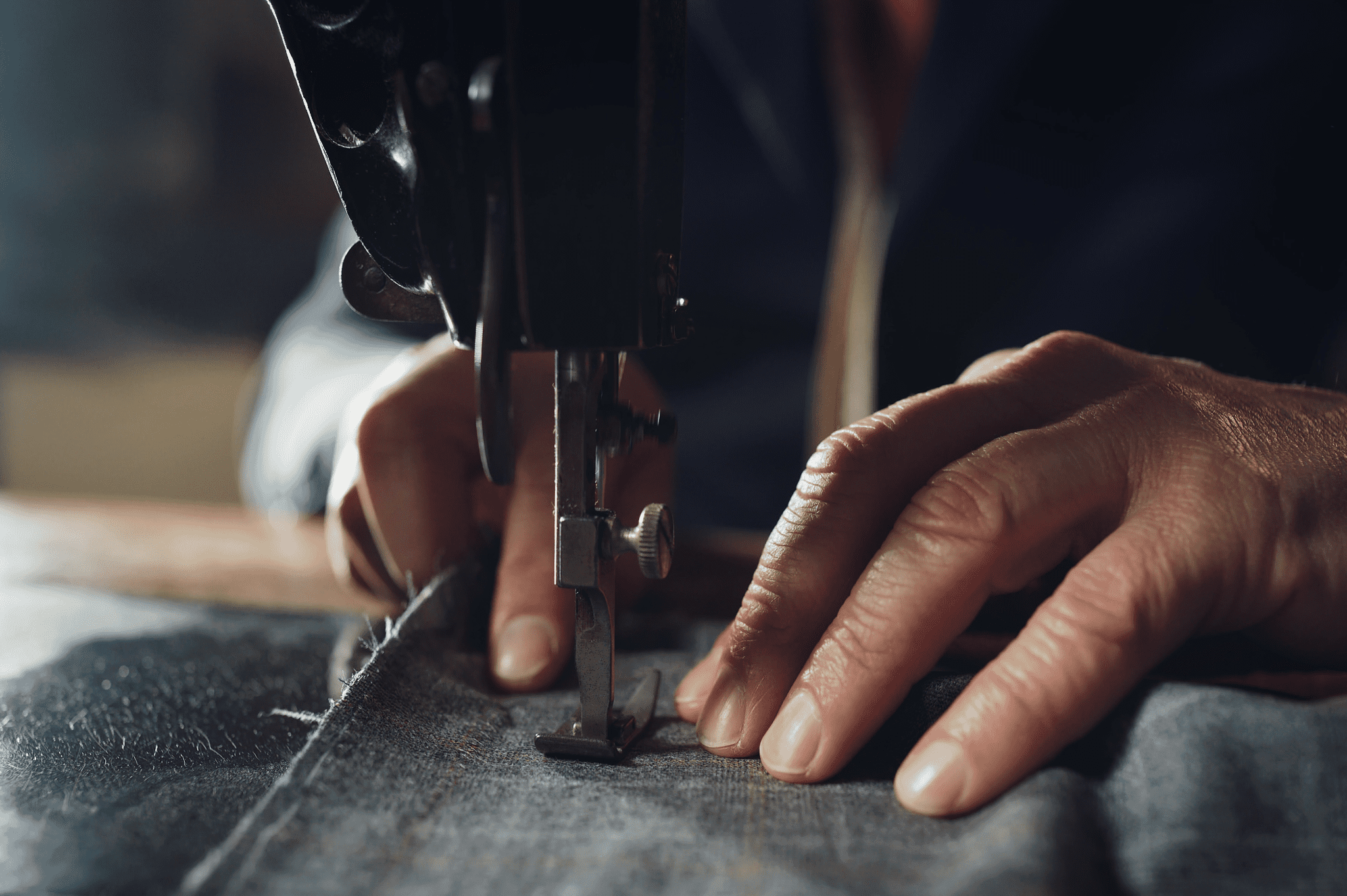 Close-up of hands guiding fabric through an industrial sewing machine, stitching a seam on a piece of denim.