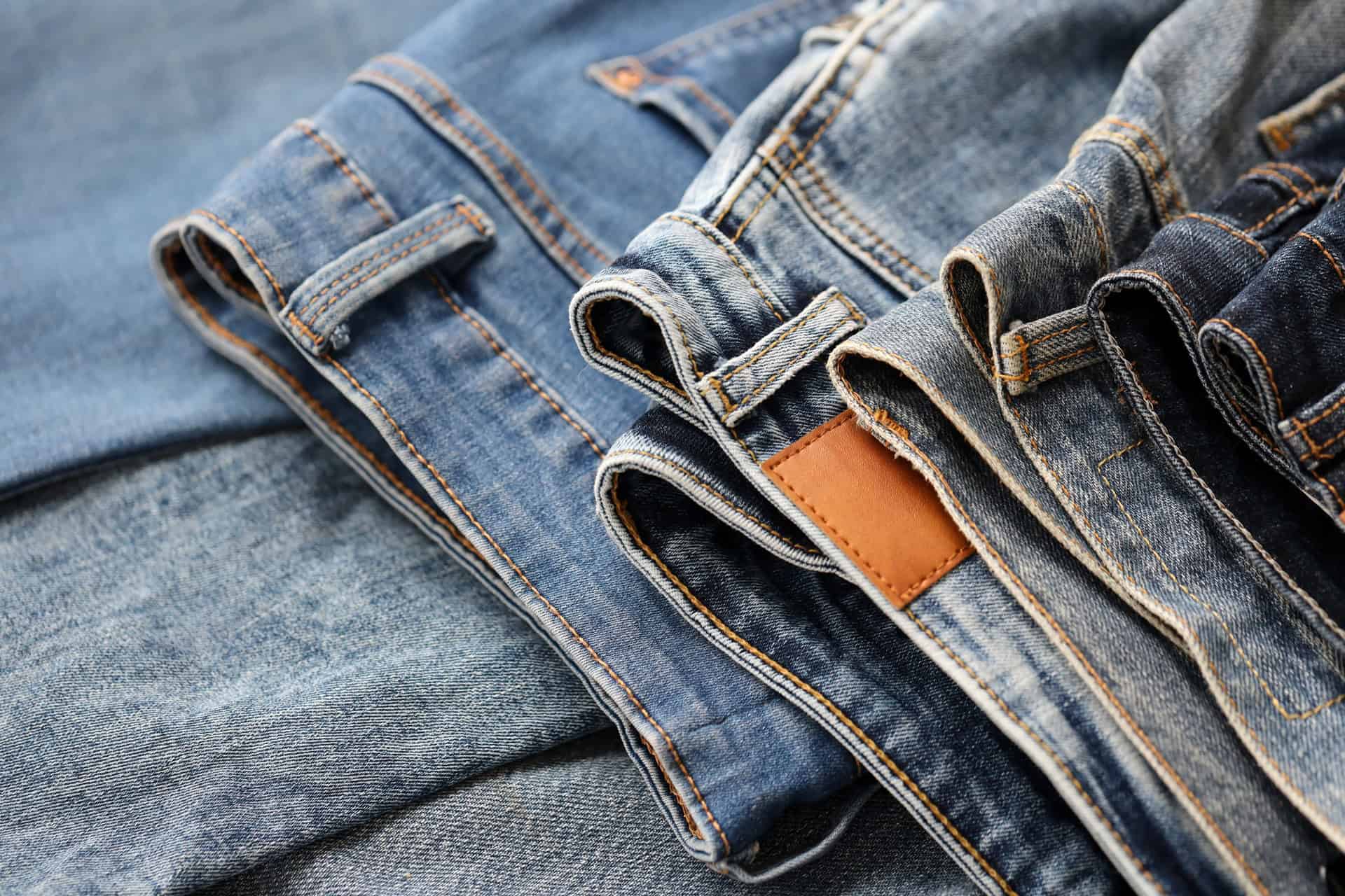 A close-up view of several pairs of blue jeans, folded and stacked side by side, showing different shades and textures of denim.