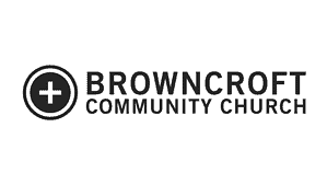 Logo for Browncroft Community Church featuring a white cross inside a black circle to the left of the church name in bold, uppercase letters.