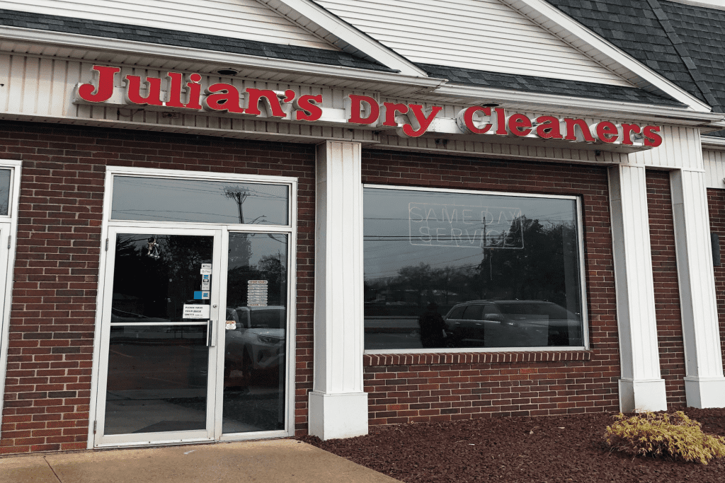 Storefront of Julian’s Dry Cleaners with large red letters above a glass door and window; “SAME DAY SERVICE” is faintly visible on the window.