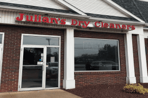 Storefront of Julian&rsquo;s Dry Cleaners with large red letters above a glass door and window; &ldquo;SAME DAY SERVICE&rdquo; is faintly visible on the window.