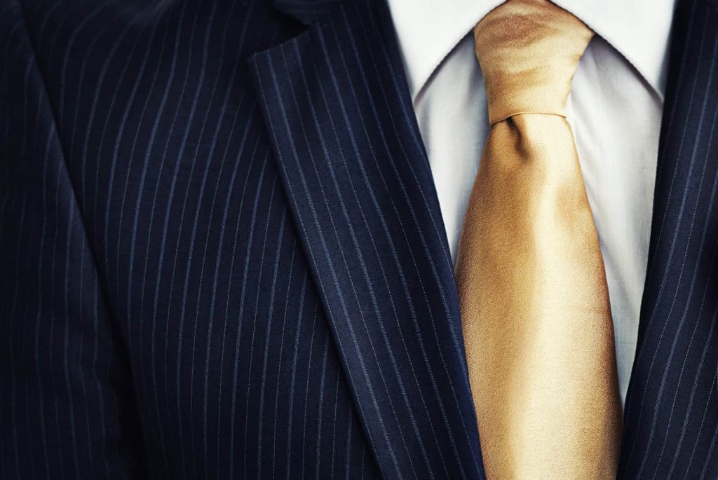 Close-up of a person wearing a dark pinstripe suit, white dress shirt, and shiny gold tie.