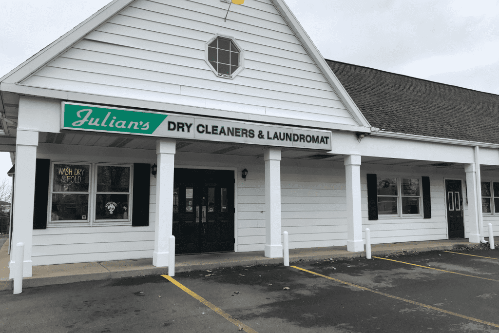 The exterior of Julian's Dry Cleaners & Laundromat, a white building with black doors and an empty parking lot.