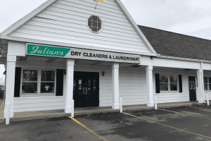 The exterior of Julian's Dry Cleaners & Laundromat, a white building with black doors and an empty parking lot.