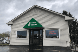 A beige one-story building with a green awning labeled "Julian's Dry Cleaners" and neon signs for "Shirt Laundry" and "Same Day Service.