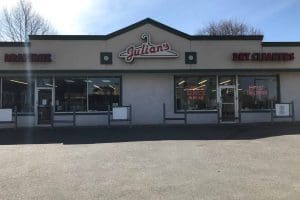 Exterior view of Julian's Dry Cleaners with signs for draperies, dry cleaning, same day service, and expert tailoring; large windows and a paved parking area in front.