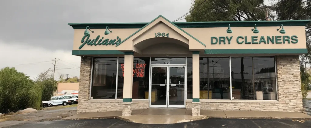 Front view of Julian’s Dry Cleaners building with glass windows, a centered glass door, and a sign displaying "1984" above the entrance.