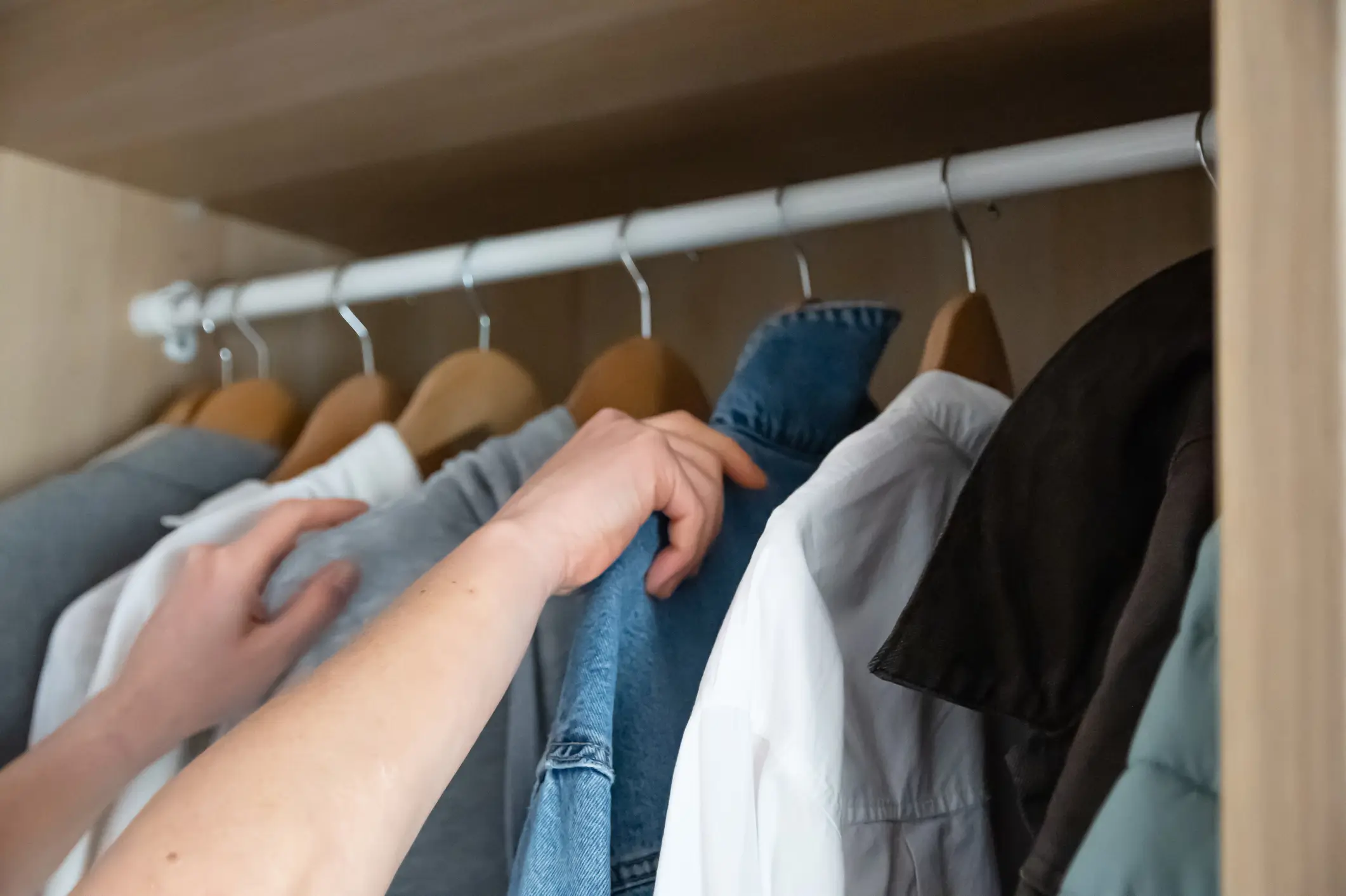 A person’s hands reach for clothes hanging on a rack in a closet.